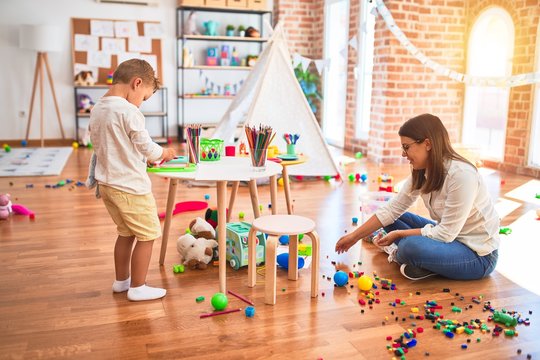 Beautiful teacher and toddler drawing using digital board around lots of toys at kindergarten