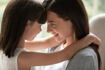 Little cute school girl touching foreheads with happy young mommy.