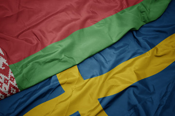 waving colorful flag of sweden and national flag of belarus.