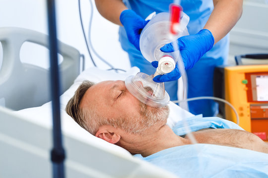 Doctors putting an oxygen mask on patient in hospital. First aid help. Reanimation room. Uncontious patient.