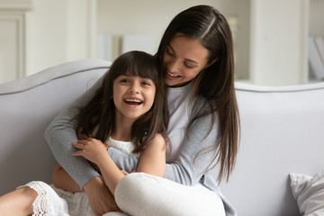 Happy young mother sitting on comfortable couch with adorable daughter.