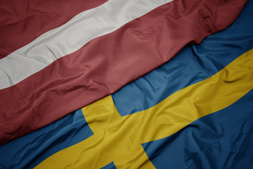 waving colorful flag of sweden and national flag of latvia.
