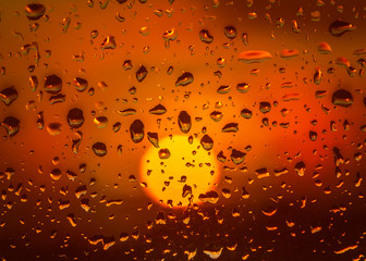 Rain drops on a window during a beautiful golden sunset. The sun is round soft focused the refelction of the sun can be seen in the rain drops.