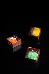 Obraz premium Art colorful chocolate candies on black background, selected focus