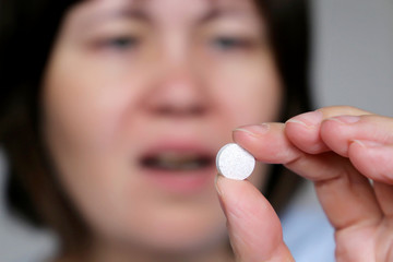 Woman taking pill, girl with open mouth holding white tablet in hand. Concept of medication,...