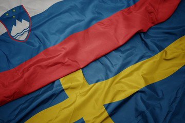 waving colorful flag of sweden and national flag of slovenia.