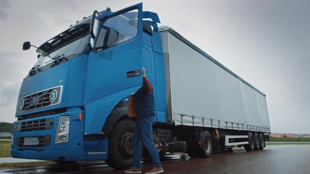 Truck Driver Crosses the Road in the Rural Area and Gets into His Blue Long Haul Semi-Truck with Cargo Trailer Attached. Logistics Company Moving Goods Across Countrie and Continent