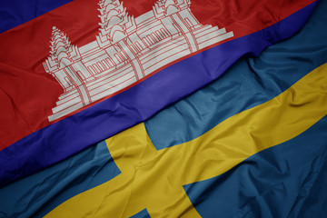 waving colorful flag of sweden and national flag of cambodia.