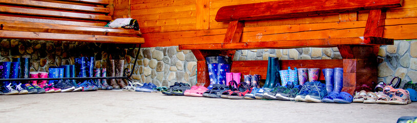 neat row of children's shoes for off-season weather under the bench - sandals, sandals, sneakers and rubber boots