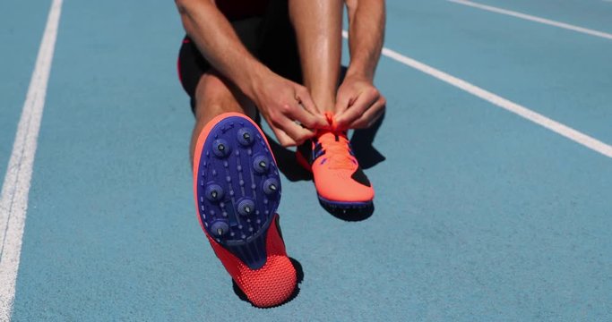 Athlete sprinter getting ready to run tying up shoe laces on stadium running tracks. Man track runner preparing for cardio training outdoors. Fitness and athletics sports. Blue background.