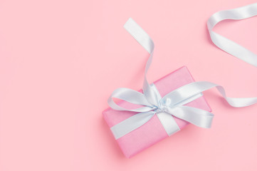 Holiday pink background with gift, white satin bow, ribbon. Valentine's Day, Happy Women's Day, Mother's Day, Birthday, Wedding, Christmas.