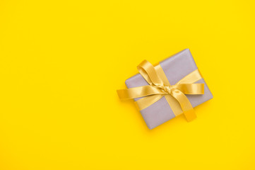 Holiday yellow background with gift, gold bow, ribbon. Valentine's Day, Happy Women's Day, Mother's Day, Birthday, Wedding, Christmas.