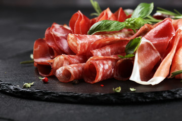 Marble cutting board with prosciutto, bacon, salami and sausages on wooden background. Rustic Meat platter