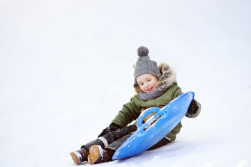 Little boy enjoy riding on ice slide in winter.