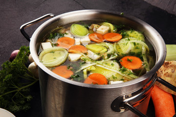 Broth with carrots, onions various fresh vegetables in a pot - colorful fresh clear spring soup....