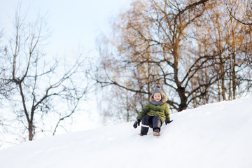 Naklejka na ściany i meble Little boy enjoying riding on ice slide in winter.