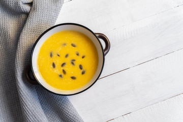 Bowl of pupkin cream soup with pumpkin seeds on white wooden table, top view
