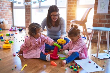 Young beautiful teacher and toddlers wearing uniform building pyramid using hoops at kindergarten