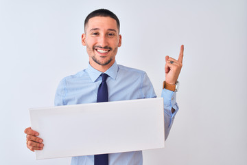 Young business man holding blank banner over isolated background very happy pointing with hand and finger to the side