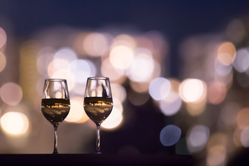 Romantic fine dinning setting. Pair of wine glasses and city night lights. 