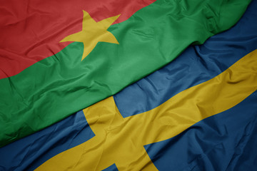 waving colorful flag of sweden and national flag of burkina faso.