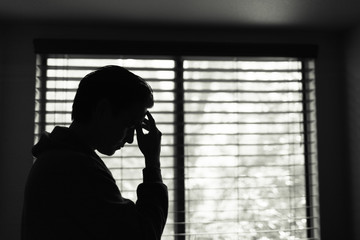 Sad man feeling, tired and stressed standing next to window. 