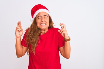 Obraz na płótnie Canvas Middle age mature woman wearing christmas hat over isolated background gesturing finger crossed smiling with hope and eyes closed. Luck and superstitious concept.