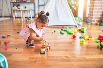 Young beautiful toddler sitting on the floor playing with wooden train toy at kindergaten