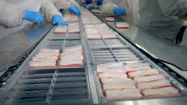 Crab sticks are getting put into plastic plates by the workers