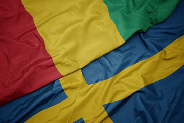 waving colorful flag of sweden and national flag of guinea.