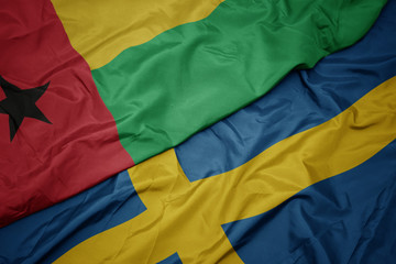 waving colorful flag of sweden and national flag of guinea bissau.