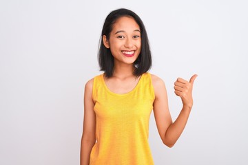 Young chinese woman wearing yellow casual t-shirt standing over isolated white background doing happy thumbs up gesture with hand. Approving expression looking at the camera showing success.