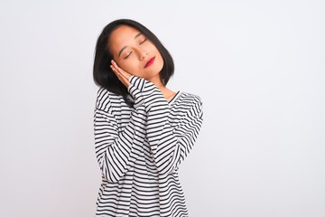 Young chinese woman wearing striped t-shirt standing over isolated white background sleeping tired dreaming and posing with hands together while smiling with closed eyes.