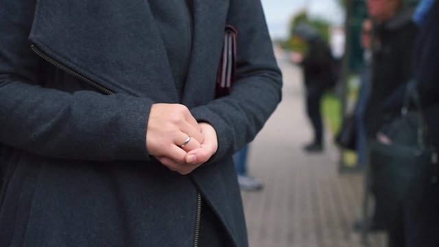 hands folded on the stomach, waiting in line at a bus stop