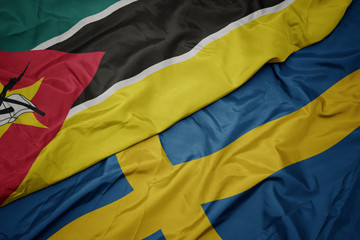 waving colorful flag of sweden and national flag of mozambique.
