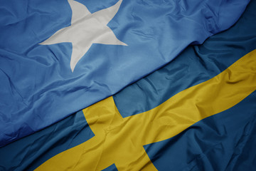 waving colorful flag of sweden and national flag of somalia.