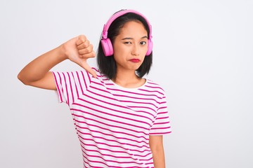 Obraz na płótnie Canvas Beautiful chinese woman listening to music using headphones over isolated white background with angry face, negative sign showing dislike with thumbs down, rejection concept