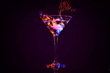 Dropping of ice cube into glass with tasty cocktail on dark background
