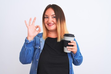 Young beautiful woman drinking take away glass of coffee over isolated white background doing ok sign with fingers, excellent symbol