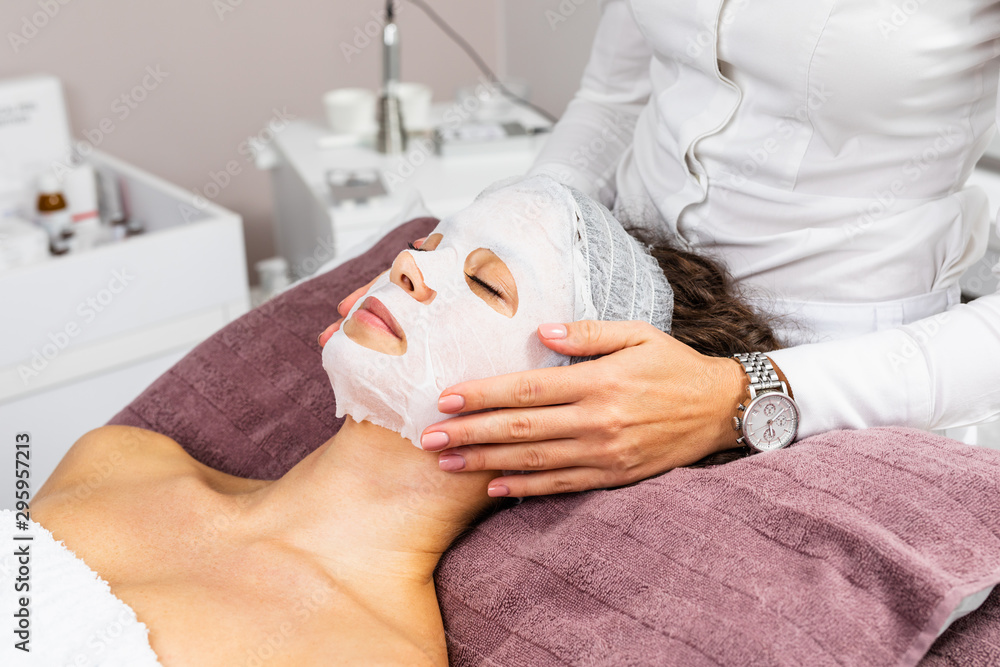 Wall mural beautiful woman receiving facial mask with rejuvenating effects in spa beauty salon.