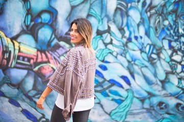 Young beautiful girl wearing grey jacket standing backwards over colorful wall  at the town street