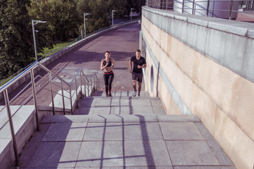 Athletic couple man woman, in summer in city, run jogging on stairs, free space for text motivation fitness and workout, sportswear. Background tiles and trees.
