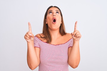 Portrait of beautiful young woman standing over isolated white background amazed and surprised looking up and pointing with fingers and raised arms.