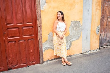 Beautiful girl leaning on orange wall, young friendly woman smiling happy on a sunny day of summer