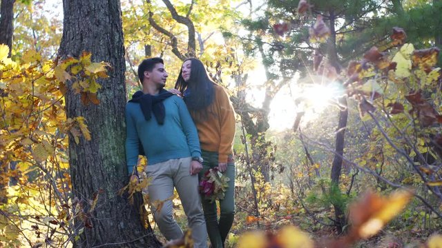 Attractive young man and woman in love are posing near big tree in sunny autumn forest