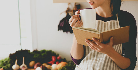 Young woman reading cookbook in the kitchen, looking for recipe