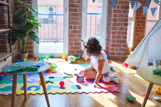 Beautiful toddler wearing glasses and unicorn diadem sitting playing with wooden building blocks at kindergarten