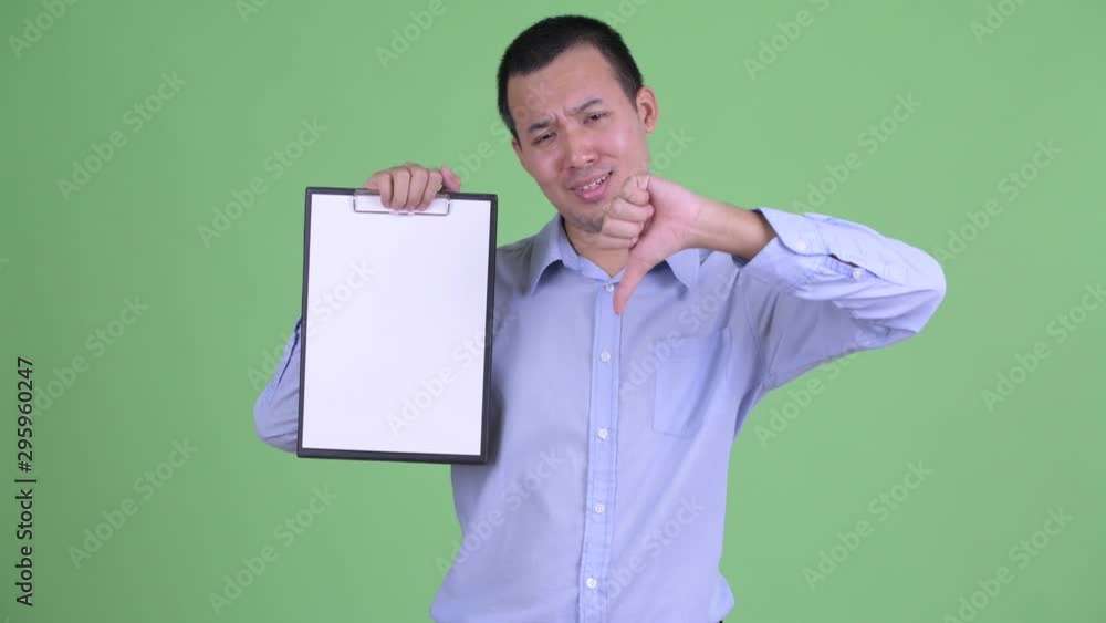 Poster Stressed Asian businessman showing clipboard and giving thumbs down