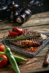 Rib eye steak on a marble plate on a wooden background. Low key, rustic style.