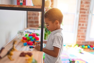 Beautiful african american toddler standing playing with small building blocks on shelving at...